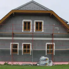 Dom w trakcie ocieplania. Szare bloczki elewacyjne, rusztowanie i materiały budowlane Austrotterm wskazują na dbałość o niski współczynnik przewodzenia ciepła.