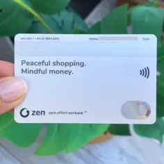 Karta zen z napisem "Peaceful shopping. Mindful money." w dłoni, na tle zielonych liści.