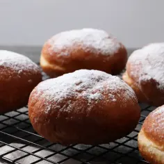 Szybkie pączki z piekarnika, oprószone cukrem pudrem, wyglądają apetycznie na czarnej kratce.