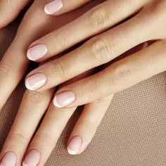 Dłonie z perfekcyjnym manicurem francuskim na jasnoróżowym tle.
