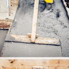 Praca przy budowie: świeży beton, z czego jest beton, wylewany do drewnianej formy. Drewniana łata rozprowadza masę.