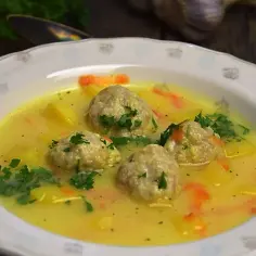 Zupa klopsowa babci: pyszne klopsiki w żółtym, kremowym sosie z ziemniakami i marchewką, posypana natką pietruszki.