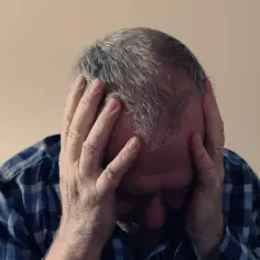 Mężczyzna z rękami na głowie, pogrążony w myślach, doświadcza trudnych emocji, być może depresji sytuacyjnej.