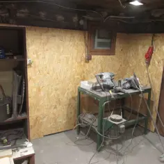 Montaż płyt OSB na ścianie w warsztacie. Na stole stoją elektronarzędzia, a obok miotła.