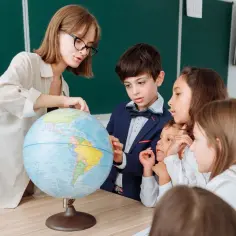 Nauczycielka pokazuje uczniom globus, wyjaśniając im świat. Dzieci z zaciekawieniem słuchają lekcji geografii.
