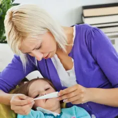 Zmartwiona mama mierzy temperaturę choremu dziecku. Warto wiedzieć, czy można kąpać dziecko z gorączką.