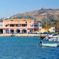 Piękna pogoda na Zakynthos we wrześniu. Port z łodziami i różowym budynkiem na tle wzgórz.