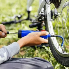 Ręce pompują koło roweru niebieską pompką. Prosty sposób, jak napompować koło w rowerze, by znów ruszyć w drogę.