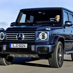 Ciemnoniebieska Mercedes G klasa na drodze. Kierowca uśmiecha się. Sprawdź aktualną mercedes g klasa cena.