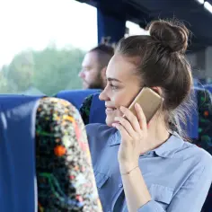 Kobieta w autobusie rozmawia przez telefon, być może szukając informacji, jak włączyć roaming Plus, by być w kontakcie podczas podróży.