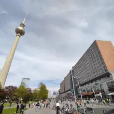 Wieża telewizyjna Berlin góruje nad placem pełnym ludzi, rowerów i budynków.
