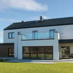 Nowoczesny dom z białymi i ciemnymi akcentami, prezentujący najmodniejsze kolory elewacji. Duże okna i szklany balkon dodają mu elegancji.