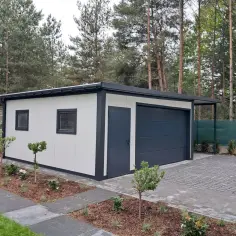 Nowoczesny garaż murowany z drzwiami i bramą garażową, otoczony zadbanym ogrodem i podjazdem z kostki brukowej.