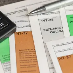 Kalkulator i długopis leżą na dokumentach PIT-37, PIT-28 i PIT-36. Czas na rozliczenie podatku i ewentualną darowiznę.