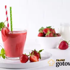 Pyszny smoothie truskawkowe w szklance z miętą i słomkami. Obok miseczka świeżych truskawek i słoik mleka.