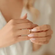 Delikatne dłonie z pastelowym manicure poprawiają złoty pierścionek zaręczynowy z brylantem. Tradycyjnie gdzie się nosi pierścionek zaręczynowy?
