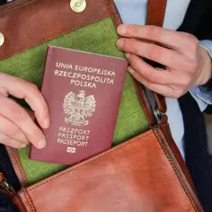 Dłonie wkładają polski paszport do brązowej torby. Czy na paszport można wziąć kredyt? To pytanie, które może pojawić się przy planowaniu podróży.