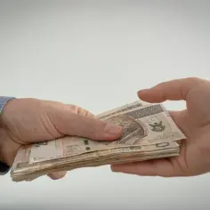 Dwie dłonie przekazujące sobie stos banknotów 200 zł.