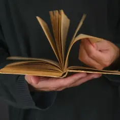 Otwarta, stara książka w dłoniach, strony lekko falują, jakby czytana była wciągająca nowela.