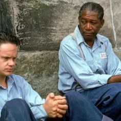 Skazani na Shawshank obsada: Tim Robbins i Morgan Freeman siedzą przy kamiennej ścianie, w więziennych strojach.