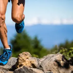 Nogi biegacza w niebieskich butach na kamienistym szlaku, pokonującego kolejne kilometry ultramaratonu.