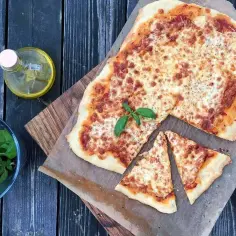 Domowa pizza Margherita z serem, bazylią i oliwą na drewnianym tle.