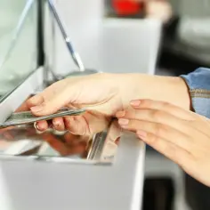Dłoń przekłada banknoty przez okienko.