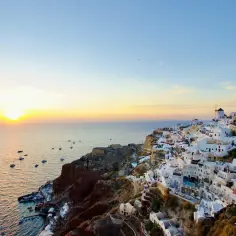 Santorini wakacje: białe domki na klifie, łodzie na morzu i zachodzące słońce. Idealny widok na wymarzone wakacje.