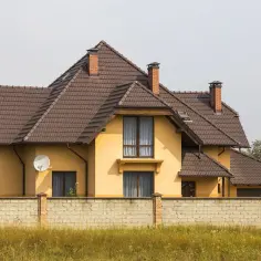 Żółty dom z brązowym dachem i ceglanym murem.