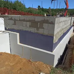 Izolacja fundamentów w starym domu w trakcie prac. Ściany z bloczków betonowych, izolacja przeciwwilgociowa i termiczna ze styropianu.