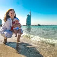 Szczęśliwa mama z dzieckiem na plaży w Dubaju, z widokiem na słynny hotel Burj Al Arab.