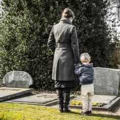 Kobieta i dziecko stoją przy grobie, przeżywając żałobę po dziadku.