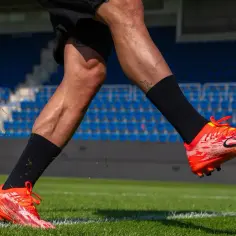 Piłkarz w pomarańczowych korkach, jakie kolki do GK, biegnie po zielonej murawie stadionu.