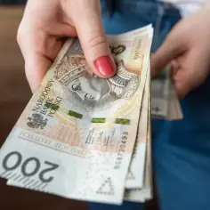 Dłoń trzyma banknoty 200 zł. Nadzieja na lepszą waloryzację rent i emerytur w 2026 roku.
