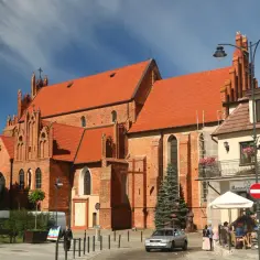 Gotycka ceglana bazylika z czerwonym dachem i błękitnym niebem.