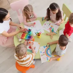 Dzieci rysują przy stole z nauczycielką. Zastanawiasz się, ile wynosi subwencja na dziecko w przedszkolu?