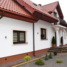 Elegancki cokół wokół domu, wykonany z brązowego tynku, chroni ściany przed wilgocią.