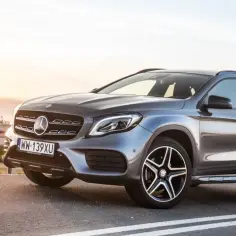 Szary Mercedes GLA 220 na tle zachodzącego słońca, zaparkowany przy drodze.