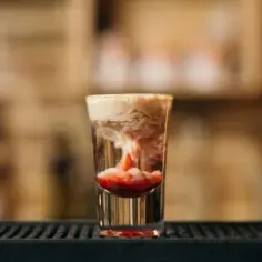 Shot "Małpi mózg" w szklance, z warstwami przypominającymi mózg i krwistą czerwienią na dnie.