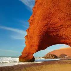 Pomarańczowe skały na plaży w Maroku, fale oceanu i błękitne niebo. Ceny w Maroku są przystępne, a widoki zapierają dech w piersiach.