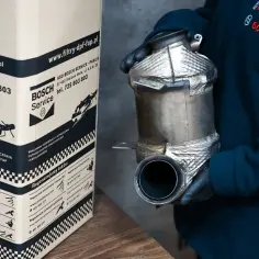 Osoba w rękawiczkach trzyma filtr DPF. Na kartonie obok widnieje napis "Pracownia regeneracji i czyszczenia filtrów cząstek stałych DPF/FAP".