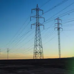 Wieże energetyczne w krajobrazie o zachodzie słońca, niosące prąd zmienny.