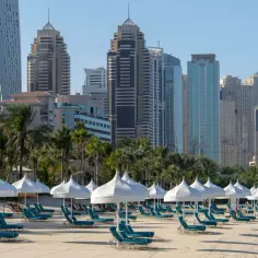 Piękna dubaj pogoda luty: pusta plaża z leżakami i białymi parasolami, w tle palmy i nowoczesne wieżowce.