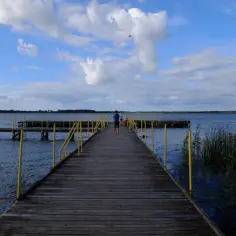 Drewniane molo nad jeziorem, z żółtymi poręczami, zaprasza do podziwiania widoków. To jedna z jezierzany atrakcji.