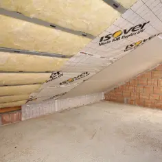 Izolacja poddasza wełną mineralną. Widoczne profile, folia paroizolacyjna Isover Vario KM Duplex UV i ceglane ściany.