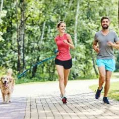 Szczęśliwa para uprawia bieganie z psem w parku. Radosny golden retriever biegnie obok nich.