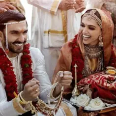 Para hinduskie wesele: pan młody w białej sherwani, panna młoda w czerwonym sari. Wskazówka, jak się ubrać na hinduskie wesele, to bogate zdobienia i żywe kolory.