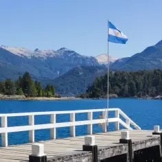 Widok na jezioro i góry w Argentynie, z białą drewnianą przystanią i flagą Argentyny. Czy Argentyna jest bezpieczna? Tak, to piękny kraj.