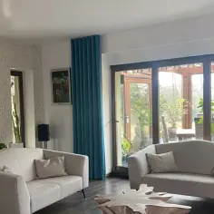 Jasne, welurowe zasłony w salonie z dwoma sofami i stolikiem kawowym.