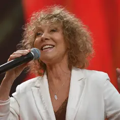 Alicja Majewska, mimo swojego wieku, wciąż zachwyca na scenie. Uśmiechnięta, z mikrofonem w dłoni, w białej marynarce.